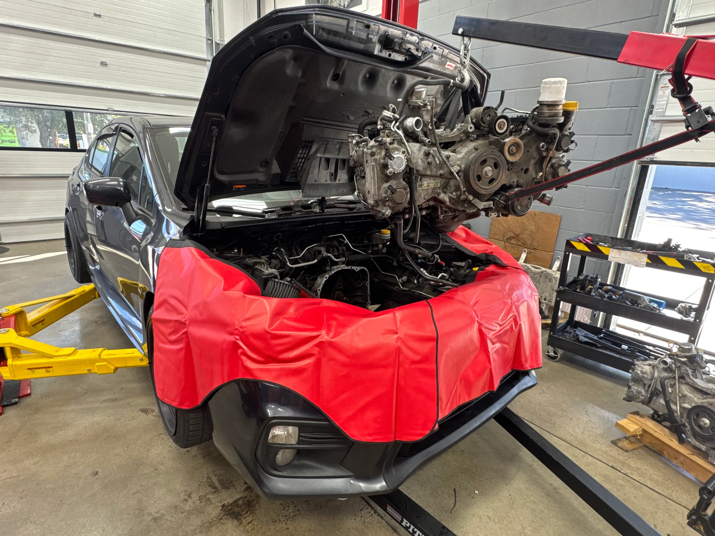 Engine suspended above an open engine bay at Fullbay Auto Centers, with a red protective apron covering the vehicle